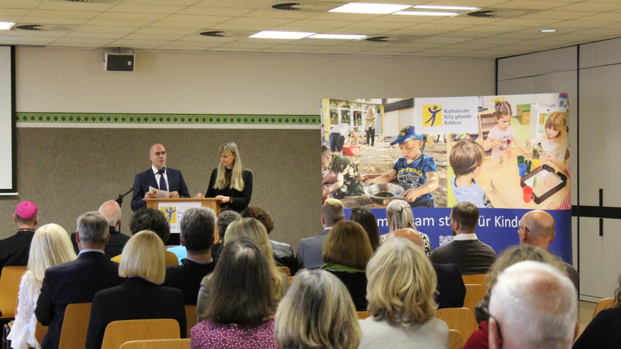 eine Frau und ein Mann, die an einem Rednerpult stehen und eine Rede halten